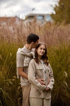 Happy couple on autumn walk outdoors. Two lovers in autumn park. Love and tender touch. Gentle hugs. Young man and woman in classic autumn colors outfit on a romantic date in a park. Young girl and guy with blond hair kisses, show love, affection. Boy and girl of European appearance with warm clothes, pictures with soft background bokeh blur fall. Concept of happiness,