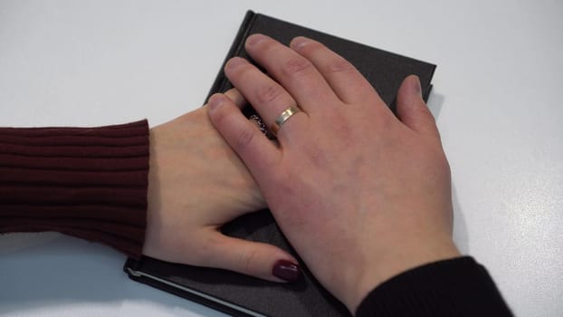 A man and a woman take an oath on the Bible. The hands of the newlyweds with rings are placed on the bible close-up. 4k