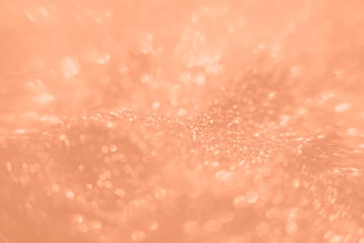 Peach Fuzz color glitter background. Blurred monochrome background with bokeh. Blurred glitters shimmering dust macro close up. High quality photo