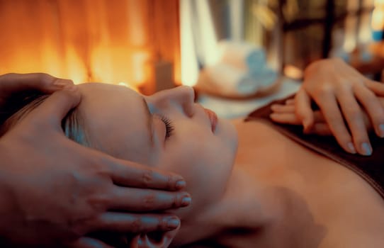 Caucasian woman enjoying relaxing anti-stress head massage and pampering facial beauty skin recreation leisure in warm candle lighting ambient salon spa in luxury resort or hotel. Quiescent