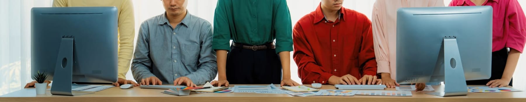 Young asian startup group works together on a project. Professional business people determine and focus on their performance while standing at office room with office equipment placed. Variegated.