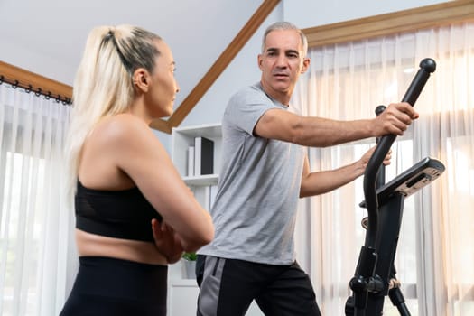 Active senior couple running on elliptical running machine at home together as fitness healthy lifestyle and body care after retirement for pensioner. Clout