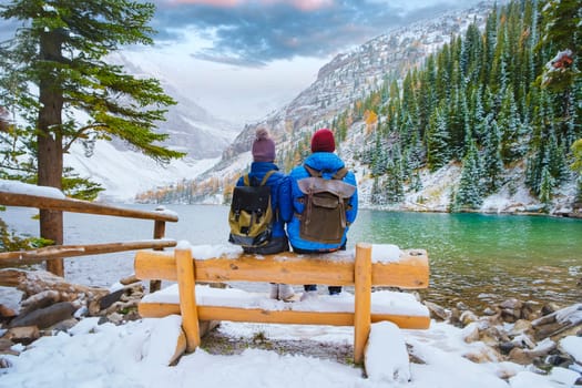 Lake Agnes by Lake Louise Banff National Park with snowy mountains in the Canadian Rocky Mountains during winter. A couple of men and women sitting on a bench by the emerald green lake in Canada with snow