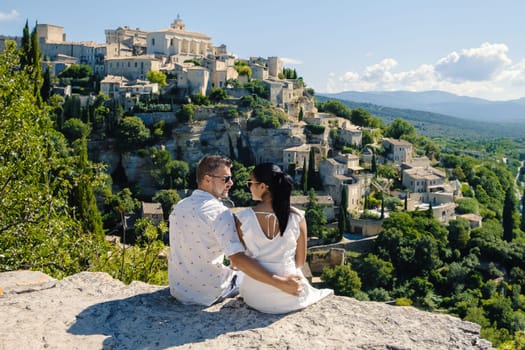 A couple of men and women on vacation in Southern France, looking out over the old historical village of Gordes Luberon Provence during summer in Europe