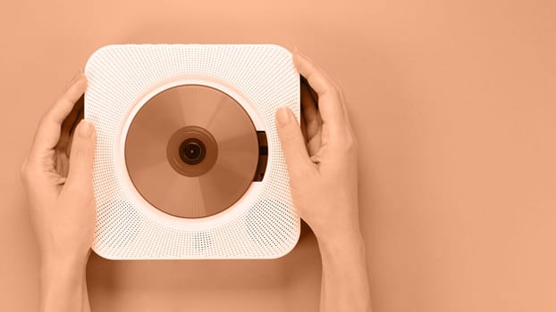 Hands holding stylish white compact CD player. Image toned in Peach Fuzz color of the year 2024. Retro vintage trending disc player. Top view, space for text