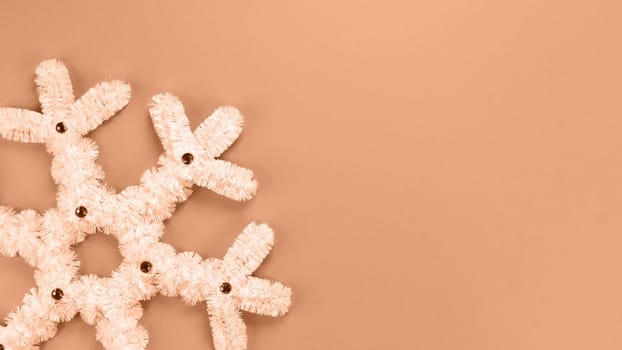 Fluffy white snowflake Christmas decor. Image toned in Peach Fuzz color of the year 2024. The concept of New Year and Christmas holidays, congratulations. Copy space. View from above.