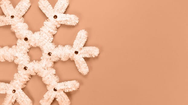 Fluffy white snowflake Christmas decor. Image toned in Peach Fuzz color of the year 2024. The concept of New Year and Christmas holidays, congratulations. Copy space. View from above.