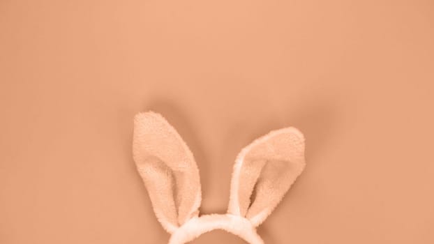 Decorative bunny ears furry fluffy costume toy. Image toned in Peach Fuzz color of the year 2024. Happy Easter concept. Simple minimalism flat lay top view copy space