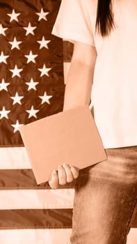 Young woman holding blank sign in her hands close up. Image toned in Peach Fuzz color of the year 2024. American flag on background