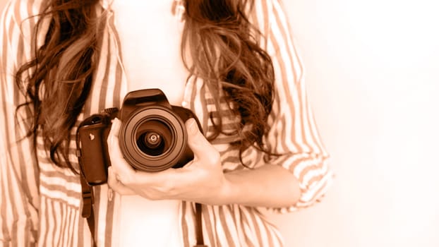 Photographer holding dslr camera. Image toned in Peach Fuzz color of the year 2024. Self portrait, front view. Faceless nice woman holding photo camera white background