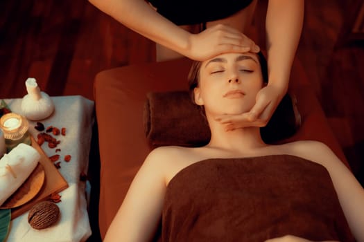 Caucasian woman enjoying relaxing anti-stress head massage and pampering facial beauty skin recreation leisure in warm candle lighting ambient salon spa in luxury resort or hotel. Quiescent