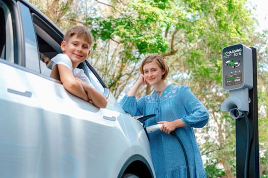 Family road trip vacation with electric vehicle, mother and son recharge EV car with green and clean energy. Nature and travel with eco-friendly car for sustainable environment. Perpetual