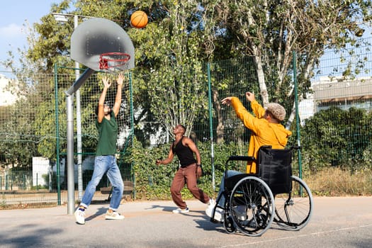 Young Black man in a wheelchair playing basketball with friends outdoors. Sports and friendship concept.
