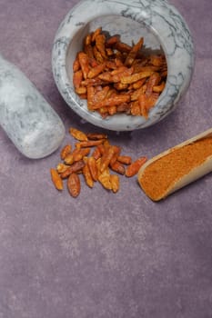 whole cayenne pepper in a white marble mortar and ground cayenne pepper in a wooden spoon.