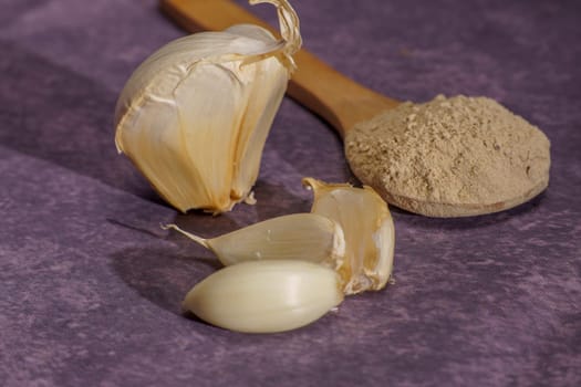 whole garlic cloves and crushed garlic in a wooden spoon