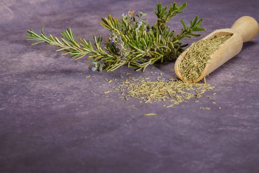 dried rosemary ground in a wooden spoon together with a branch of fresh rosemary blossoms