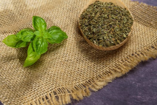 dried basil ground in a wooden spoon with freshly cut basil leaves on a burlap cloth