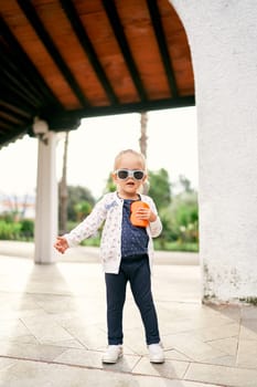 Little girl in sunglasses stands on a tile in a pergola in the garden. High quality photo