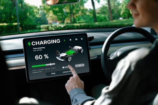 Electric car driver checks battery charging status, range and charging limit on app screen in the car. Smart technology device show EV car recharging data of electric storage in car battery innards.