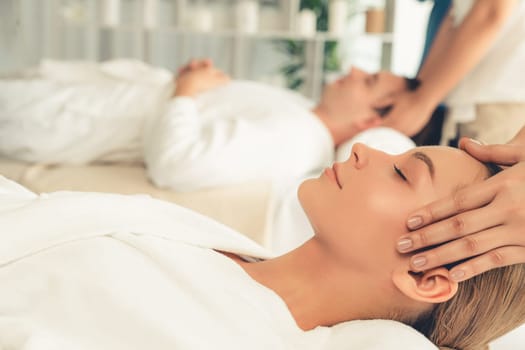 Caucasian couple enjoying relaxing anti-stress head massage and pampering facial beauty skin recreation leisure in dayspa modern light ambient at luxury resort or hotel spa salon. Quiescent