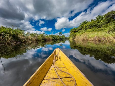 Tranquil river mirrors the sky from a yellow canoe's prow.