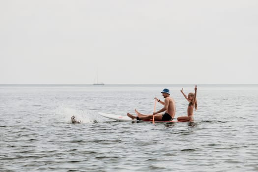 Father and his adorable little son and daughter sitting on stand up board having fun during summer beach vacation