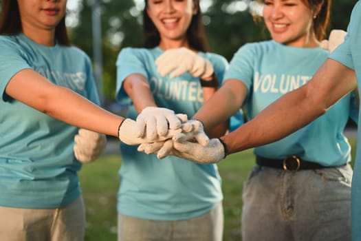 Group of young volunteers stacking hands together showing teamwork spirit. Charity and ecology concept.