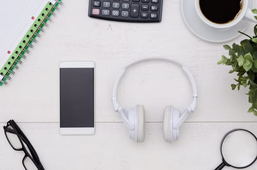 Office desk table layout with headphones and smartphone. Flat lay listening music composition on white wooden background