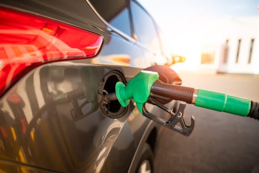 Gas pump nozzle in the fuel tank of a gray car. Refueling the vehicle at a gas station