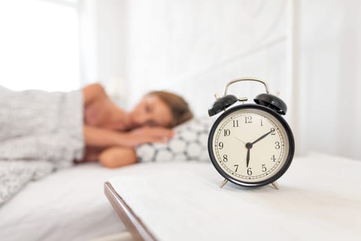 Young woman is sleeping in her bed. Alarm clock in the foreground