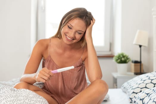 Young happy woman because of the pregnancy test result. Woman holding a pregnancy test in hands