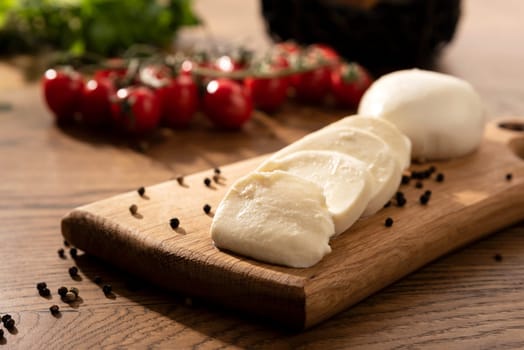Mozzarella cheese on wooden chopping board. Cherry tomatoes in background. Wooden table with Italian food composition