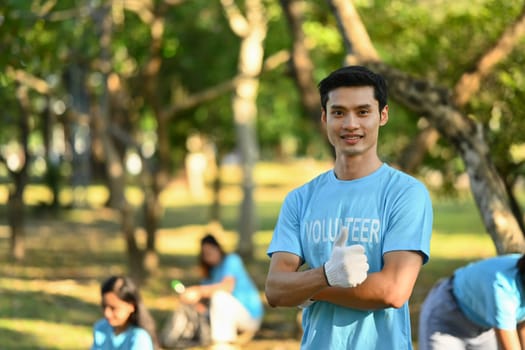 Positive male volunteer in blue uniform smiling at camera while standing outdoor. Charity and community service concept.