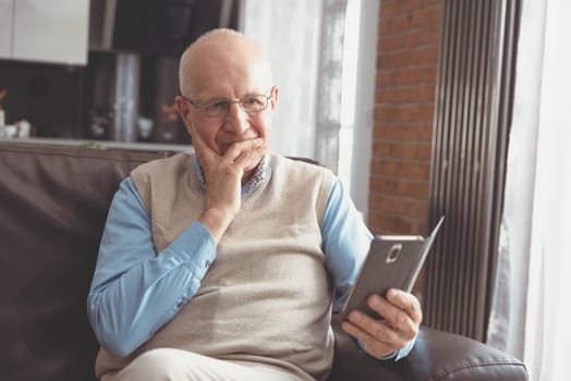 Senior man using a smartphone and smiling while sitting on couch at home.