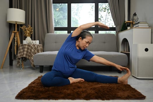 Active middle age woman doing stretching exercise in living room at home. Healthy lifestyle concept.