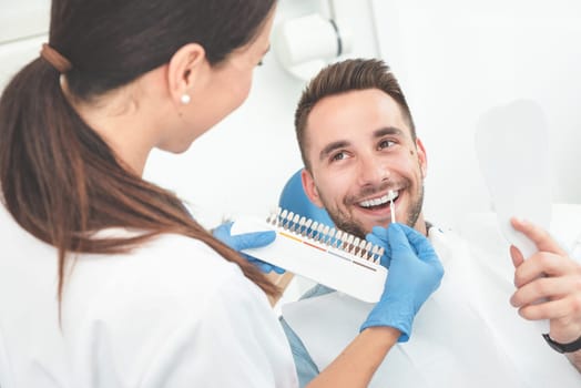 Handsome young man in stomatology clinic with female dentist. Healthy teeth whitening.