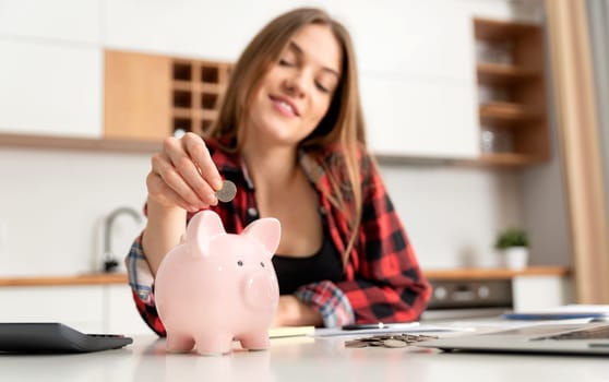 Woman putting money into piggy bank at table. Home budget concept