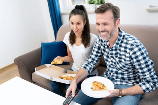 Couple watching TV while eating pizza. Spending free time at home