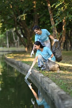 Happy young volunteer women collecting trash in the public park. Environmental protection and charity concept.