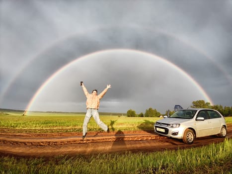 An adult girl in a field with a stormy sky with clouds and grey rainbow. Woman having fun outdoors on rural and rustic nature near car. The Grey Rainbow and the Ban on LGBT symbols in Russia