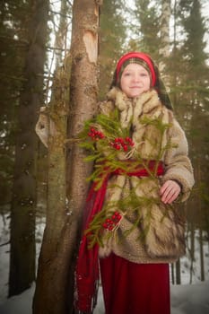 Portrait of Teen girl in coat, red sash and branch of fir tree with bright berries in cold winter day in forest. Medieval peasant girl with firewood. Photoshoot in stile of Christmas fairy tale