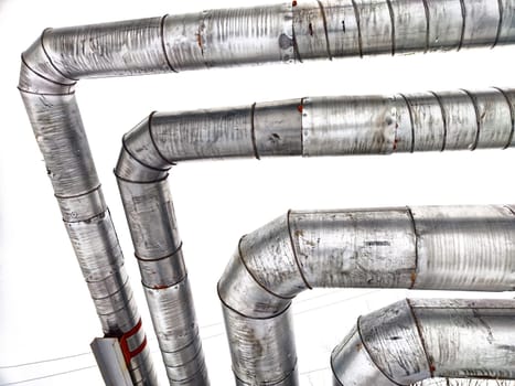 Metal pipes in thermal insulation winding outdoors and the over-illuminated white sky on background