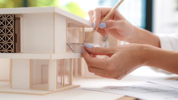 Closeup image of young beautiful caucasian architect engineer hand measure house length model by using ruler and pencil at modern office. Creative house design concept. Focus on hand. Immaculate.