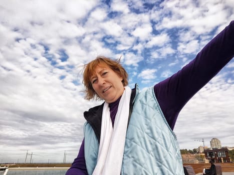 Happy, funny, funny adult girl takes a selfie against a blue sky with white clouds. A middle-aged woman poses on the phone in nature in autumn or spring