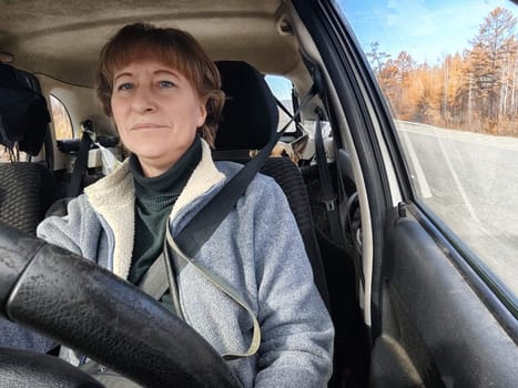 Portrait of female driver in solo journey. Adult mature woman holding steering wheel and looking through windscreen in travel by vehicle on vacation. Lady girl who is owner or rent car for travel