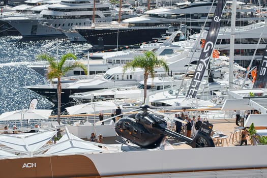 Monaco, Monte Carlo, 27 September 2022 - Rich clients visitors examine a helicopter standing on the deck of a yacht club, the largest fair yacht show, port Hercules, yacht brokers, sunny weather. High quality photo