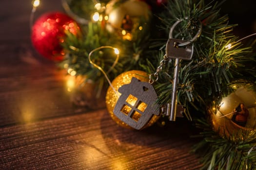 Gift key house with a keychain backdrop of Christmas tree. Building, design, project, moving to new house, mortgage, rent and purchase real estate. A gift for New Year, Christmas.