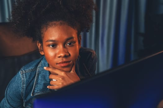 Young African American creator woman with serious face, thinking carefully and looking at final project document on laptop for planing next sequence. Concept of work at neat home place. Tastemaker.