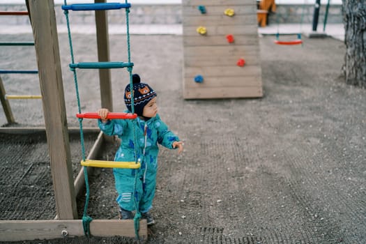 Little girl stands near a rope ladder and looks away. High quality photo