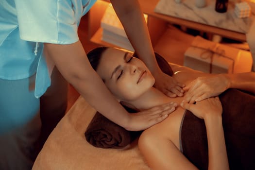 Caucasian woman customer enjoying relaxing anti-stress spa massage and pampering with beauty skin recreation leisure in warm candle lighting ambient salon spa at luxury resort or hotel. Quiescent